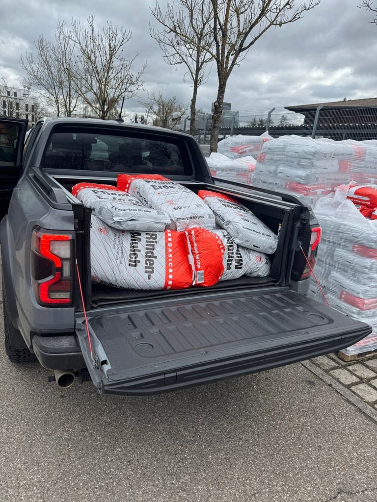 Pickup truck bed loaded with white bags of building materials with red and white branding, parked at an industrial site